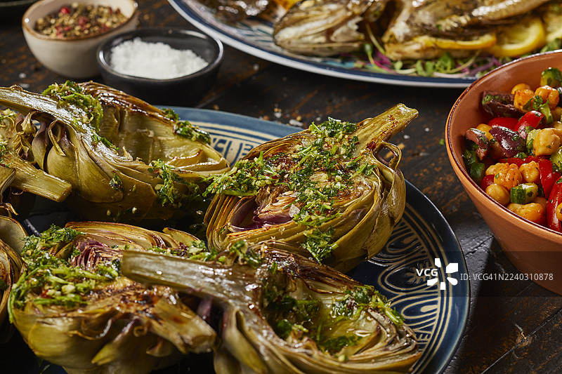 烤朝鲜蓟对半切开，配有奇米奇里酱，盛放在盘子里。图片素材