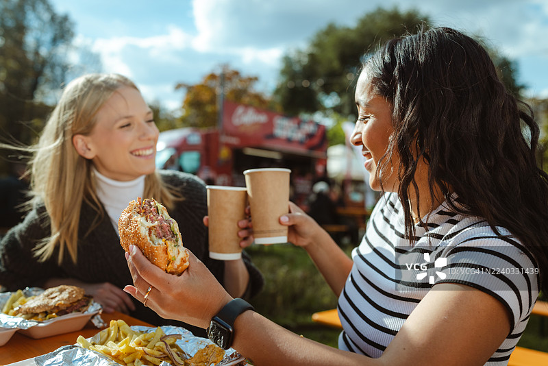 两位朋友在户外街头节上，一边享用外卖美食，一边开怀畅饮。图片素材