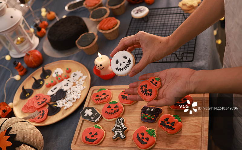 特写一位女士的手，手中拿着装饰成橙色南瓜的万圣节饼干，一位家庭主妇正在为万圣节活动准备蛋糕和饼干。图片素材