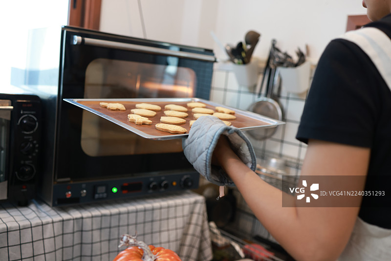 特写：女性饼干蛋糕店老板制作万圣节南瓜蛋糕，周围装饰着万圣节饰品。图片素材