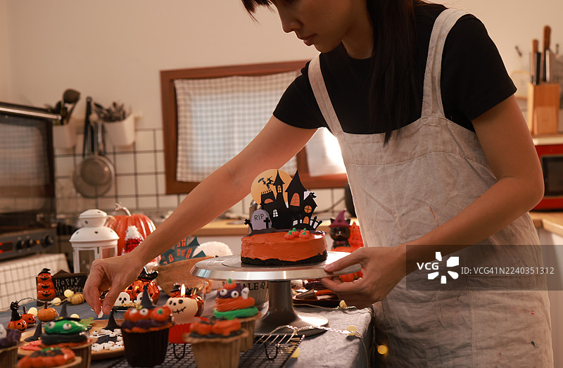 特写：女性饼干蛋糕店老板制作万圣节南瓜蛋糕，周围环绕着万圣节装饰。图片素材