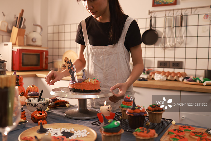 特写：女性饼干蛋糕店老板制作万圣节南瓜蛋糕，周围是万圣节装饰。图片素材