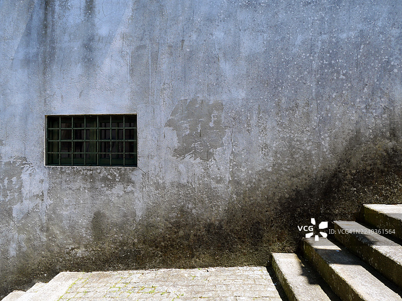 葡萄牙波尔图，布满灰尘的水泥墙，刷着蓝色油漆，饱经风霜，还有一个带栅栏的窗户。石头楼梯。阳光。自然色彩。图片素材
