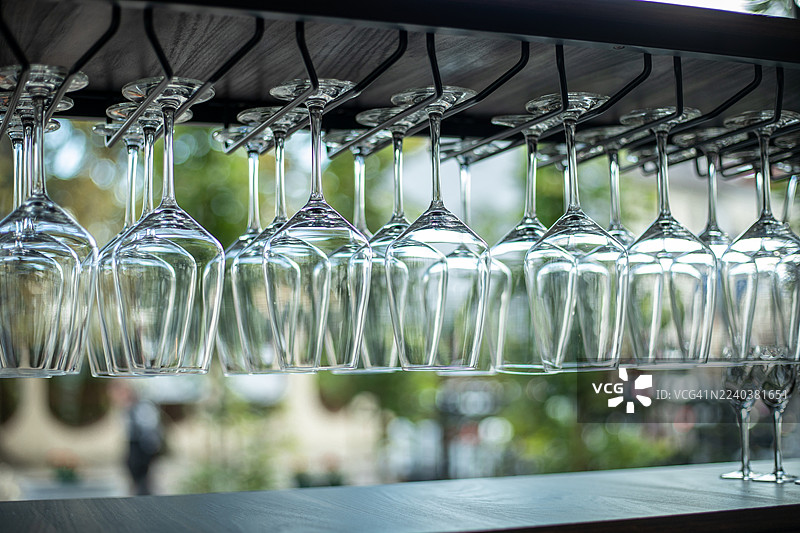 现代咖啡馆或餐厅内部，吧台上方倒挂着一排空的水晶酒杯。透明的玻璃器皿反射着自然日光，构图优雅，背景柔焦。图片素材