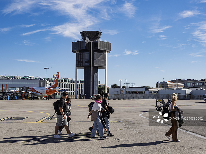 一群乘客在瑞士日内瓦国际机场航站楼外带着随身行李下飞机。图片素材