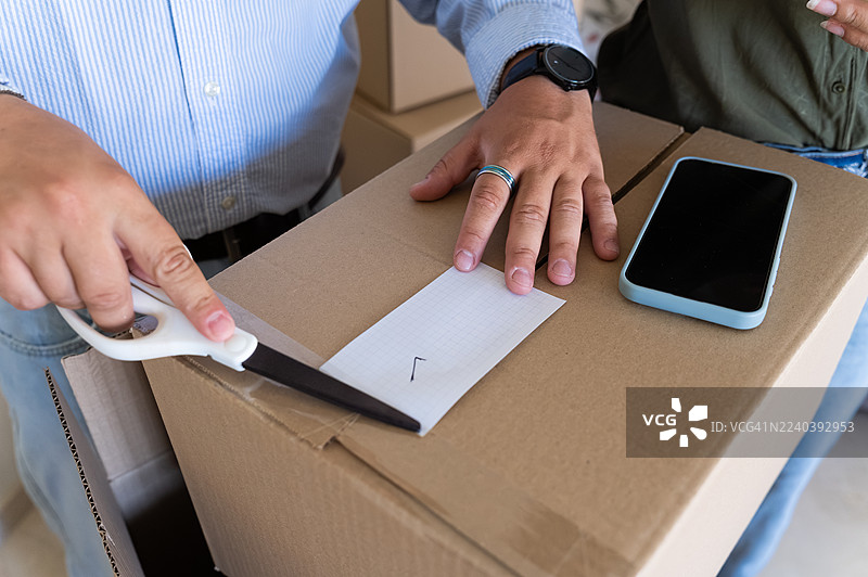 网上卖家正在用剪刀剪一个包裹的运输标签图片素材