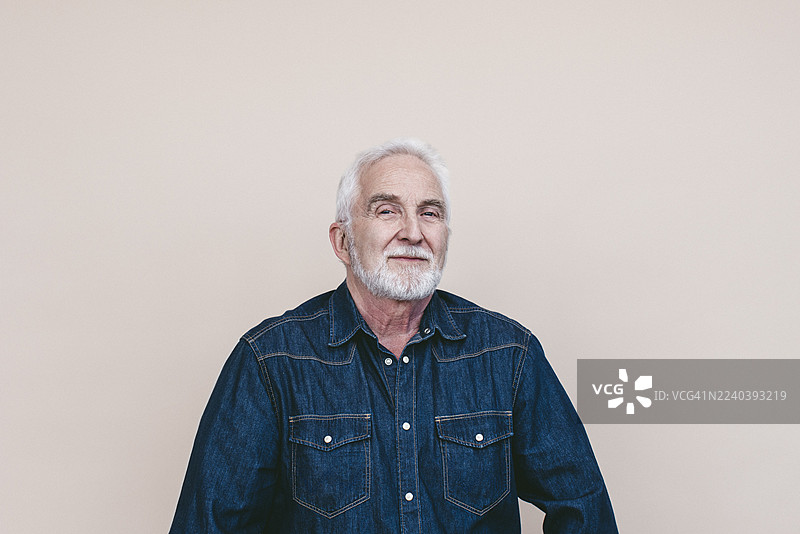自信的年长男子身穿牛仔夹克，在奶油色背景前拍摄肖像照图片素材