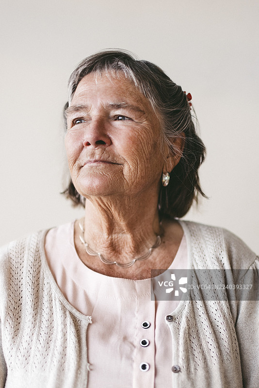 一位沉思的老年女性，背对彩色背景望向别处。图片素材