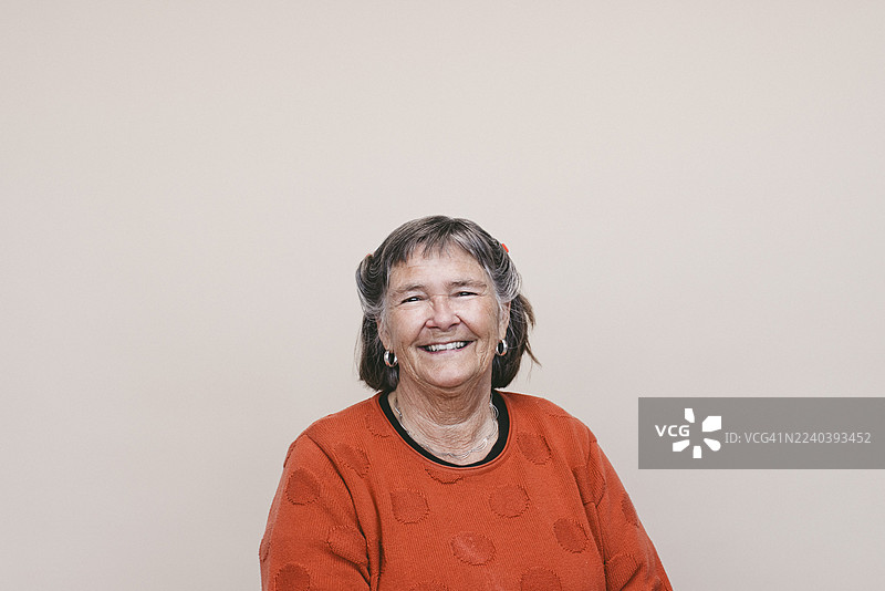 一位穿着红色上衣的快乐老年女性肖像，背景为米色图片素材