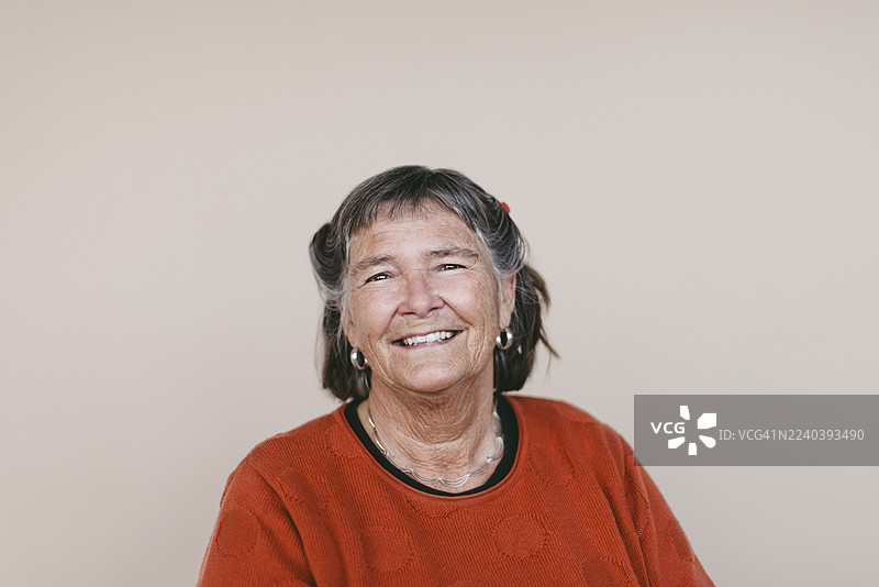 一位微笑的短发老年女性的肖像，背景为米色图片素材