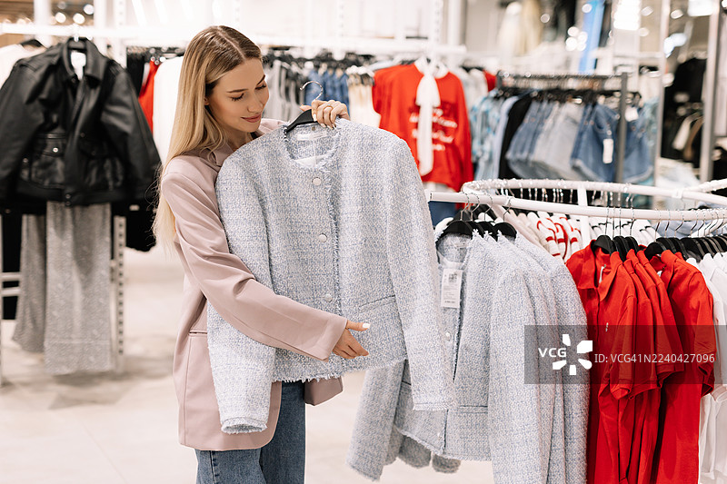 年轻时尚的购物狂女性在商场店铺试穿并购买衣物。明亮店内的消费主义和零售疗法概念。图片素材