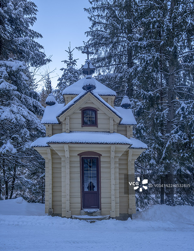 宁静的常绿森林中矗立着一座小木质东正教教堂，覆盖着新鲜的积雪，营造出一种宁静的冬日景象，融合了宗教建筑和自然之美。图片素材