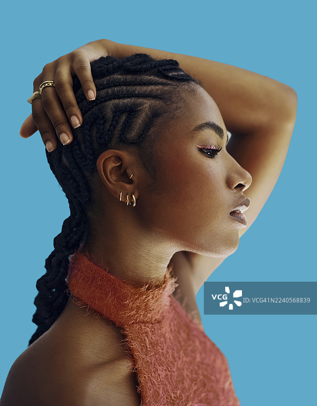 身穿红色服装、留着编织发型的黑人女性在蓝色背景前沉思地摆姿势。图片素材