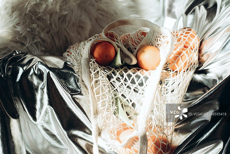 橘子放在网袋里，背景为银色。现代风格。迪斯科风格。现代时尚静物。图片素材