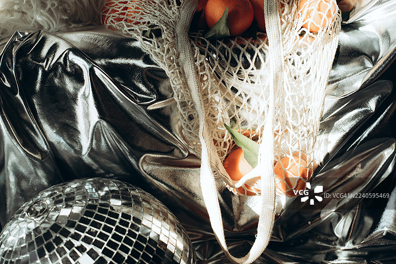 橘子放在网袋里，背景为银色。现代风格。迪斯科风格。现代时尚静物。图片素材