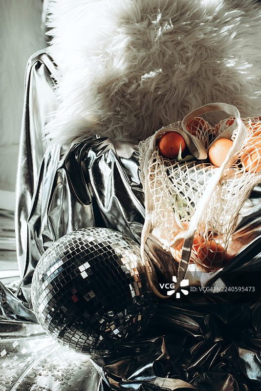 橘子放在网袋里，背景为银色。现代风格。迪斯科风格。现代时尚静物。图片素材