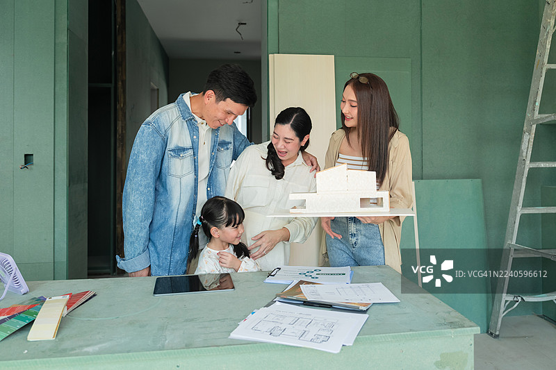 亚裔女性室内设计师正在与家庭客户就房屋翻新进展进行咨询，讨论新房室内改造项目的施工细节、设计改进和搬迁计划。图片素材