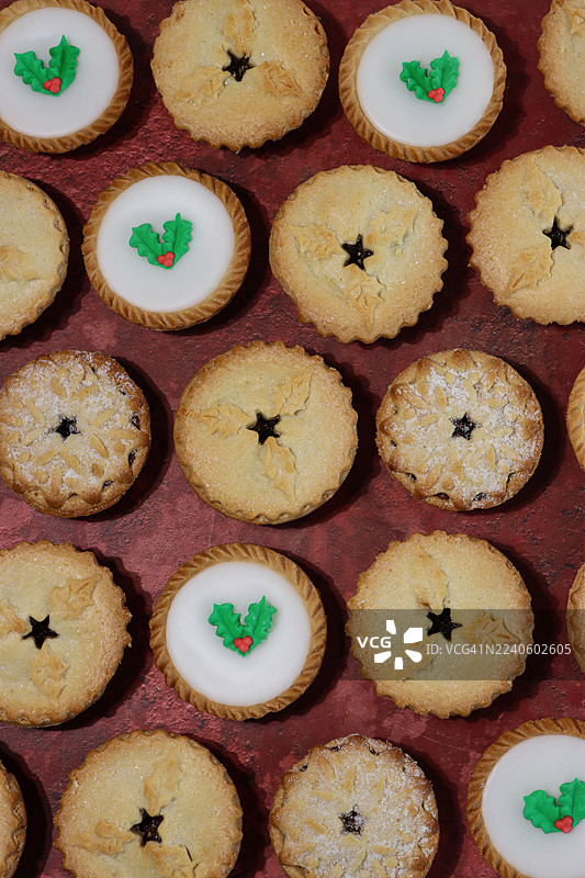 全画幅俯拍图，手工制作的圣诞肉馅饼，顶部有星星状酥皮盖或白色糖霜覆盖，并饰有绿色和红色的冬青叶和浆果，节日圣诞甜点，脆皮酥皮包裹着甜肉馅，撒上糖粉。图片素材