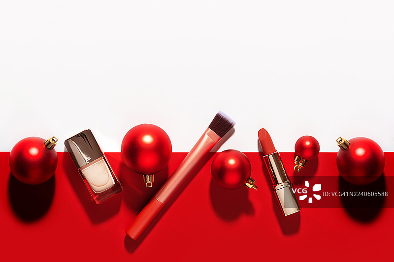 圣诞装饰红色圣诞树挂饰与美妆产品摆放在红白色背景上。图片素材