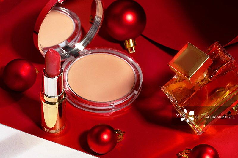 为女性准备的节日或礼物的概念，由美容化妆品制成，带有苛刻的光线效果、圣诞树装饰品和红白背景上的阴影。图片素材