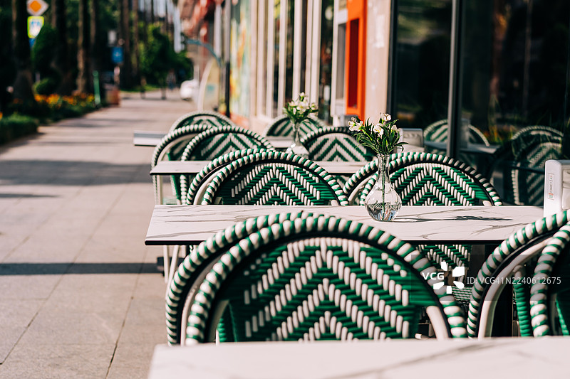户外咖啡馆座位，配有绿白条纹椅子和装有鲜花的小玻璃花瓶图片素材