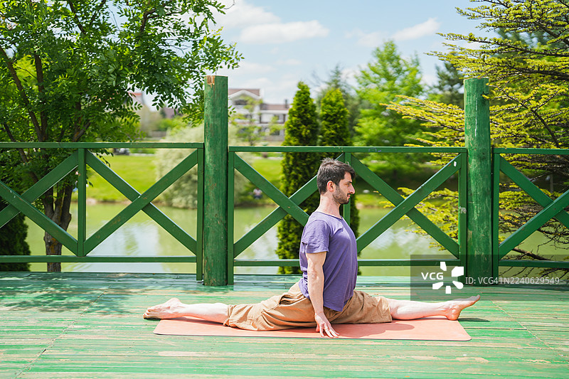 男人在户外木制甲板上练习前水平劈叉瑜伽体式图片素材