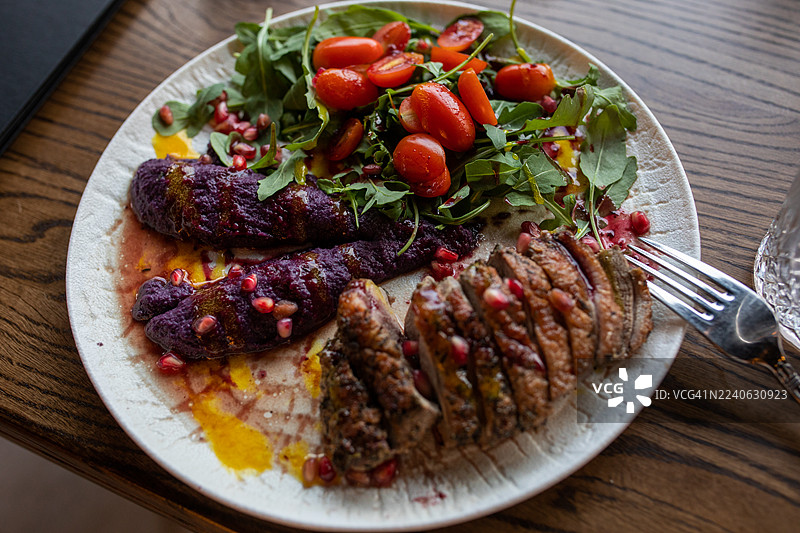烤肉片、甜菜根、新鲜蔬菜、番茄、石榴和沙拉的精致菜肴图片素材