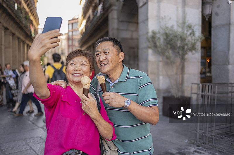 成熟的亚洲夫妇在度假时一边吃冰淇淋一边自拍。图片素材
