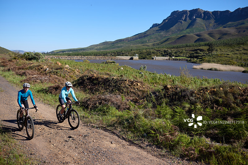两位骑行者骑着砾石自行车，沿着西开普省的山脉，在风景优美的保护区内骑行。图片素材