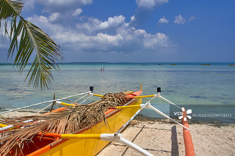 一艘色彩鲜艳的黄色和橙色巴卡船，一种菲律宾传统的支腿船，静静地停靠在白色的沙滩上。图片素材