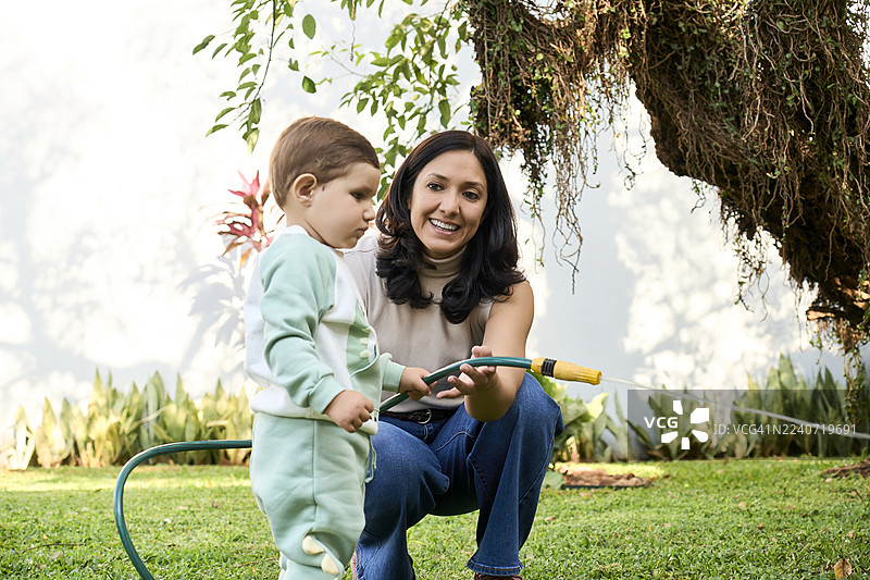 母亲在花园里帮助儿子浇灌植物图片素材