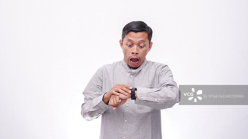 震惊的亚洲男子在白色背景下看着他的智能手表图片素材