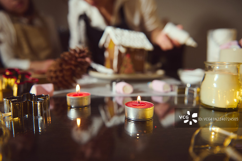 玻璃桌上的蜡烛，配有姜饼屋和温馨的节日气氛图片素材