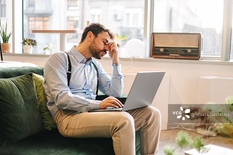 疲惫的男人在共享办公空间用笔记本电脑工作时揉眼睛图片素材