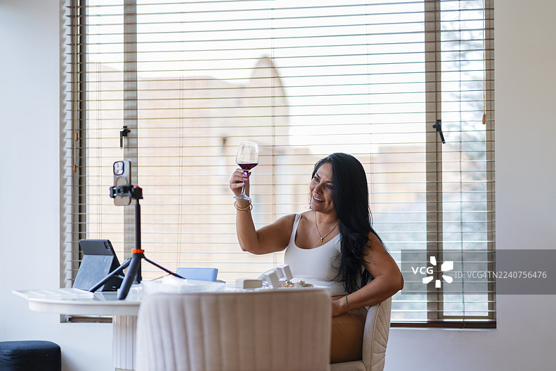 一名女子通过视频通话洽谈她的珠宝，在镜头前展示宝石，并一边交易一边品酒。图片素材