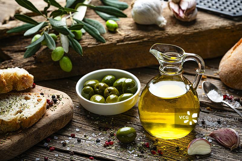 地中海美食：特级初榨橄榄油瓶和绿色橄榄放在质朴的木桌上。胡椒、盐和大蒜。美味佳肴图片素材