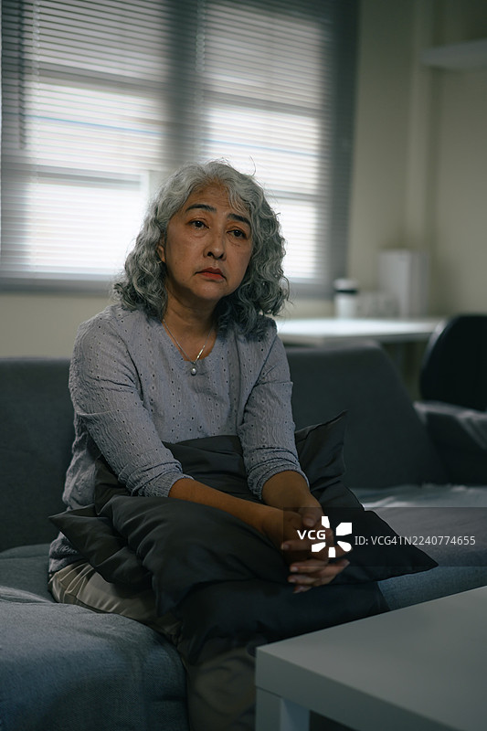 一位年长的亚洲女性独自在家中静坐，在自然光下陷入沉思图片素材