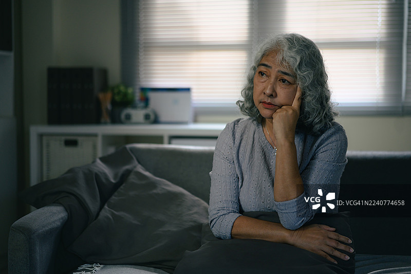 一位年长的亚洲女性独自在家中静坐，在自然光下陷入沉思图片素材