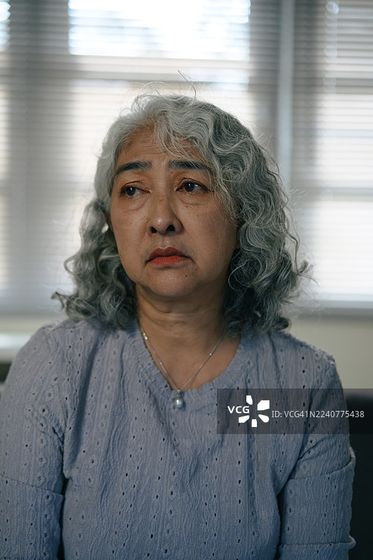 一位年迈的亚洲女性独自在家中静坐，在自然光下陷入沉思图片素材
