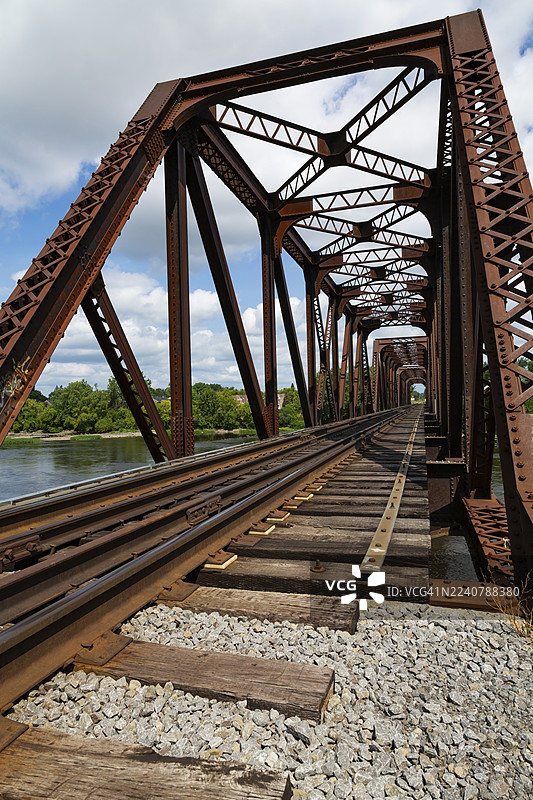 夏季,加拿大魁北克省拉瓦尔市,特尔博讷普拉特桁架老式生锈铁路桥横跨德米勒岛河,铁轨通向桥梁。图片素材