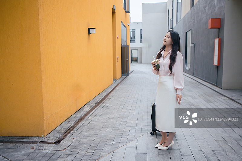 亚洲女商人出差旅行，走在黄色墙壁的街道上寻找酒店。专业的女企业家携带行李，探索城市环境，图片素材