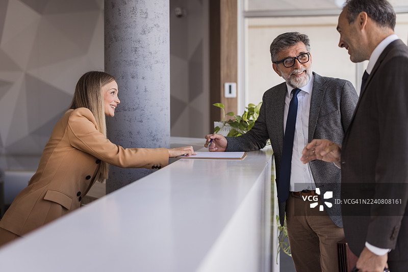 接待员协助下，商务人士在接待处签署文件图片素材