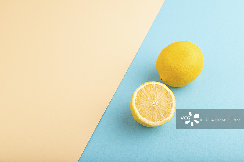 背景为橙色和蓝色柔和色纸的对半切开的黄柠檬。侧视图，平铺，留有复制空间。健康食品，蔬菜，极简主义图片素材