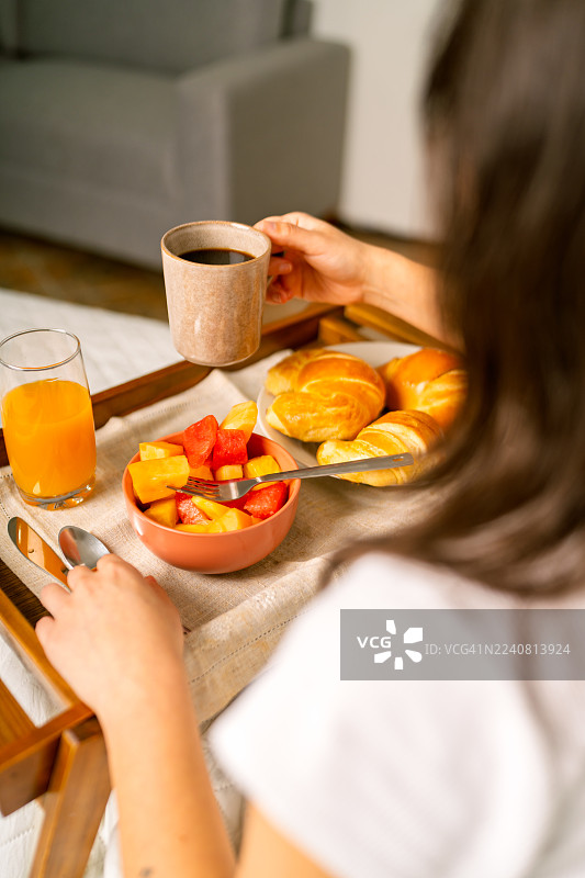 女人在床上享用早餐，配有咖啡和水果沙拉。图片素材