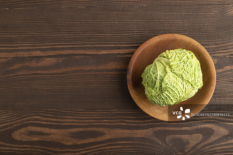 绿色生菜在盘子里，背景为棕色木纹。俯视，留白，简约风格。健康食品，蔬菜，极简主义。图片素材