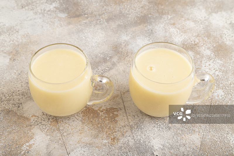 棕色混凝土背景上的有机非乳制香蕉豆奶，装在玻璃杯中。素食健康食品概念，侧视图，特写。图片素材