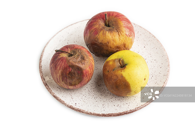 陶瓷盘中腐烂、变质的苹果，孤立在白色背景上。侧视图，留白，极简主义图片素材
