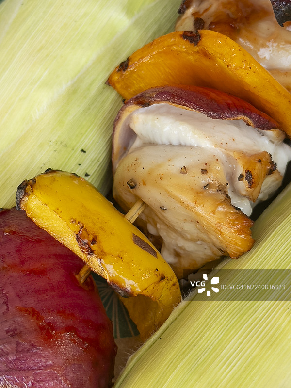 烤架上烤好的烤鸡肉串，旁边放着两个玉米棒，特写，红、黄、橙色的甜椒，洋葱，系列中的一部分图片素材