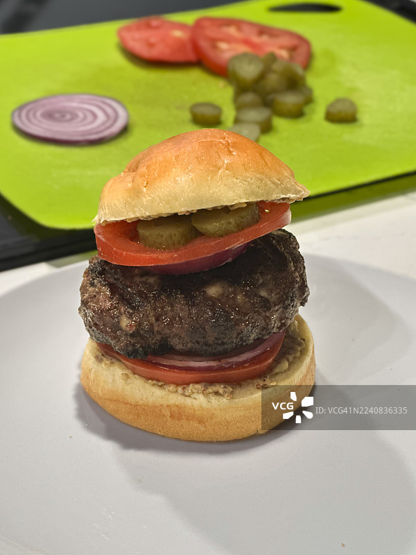 高叠的熟牛肉汉堡，夹有番茄、洋葱、酸黄瓜和褐色芥末酱，属于系列图。图片素材