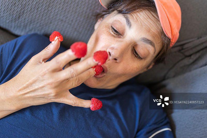 一位成熟的女性在沙发上俏皮地吃着新鲜覆盆子图片素材